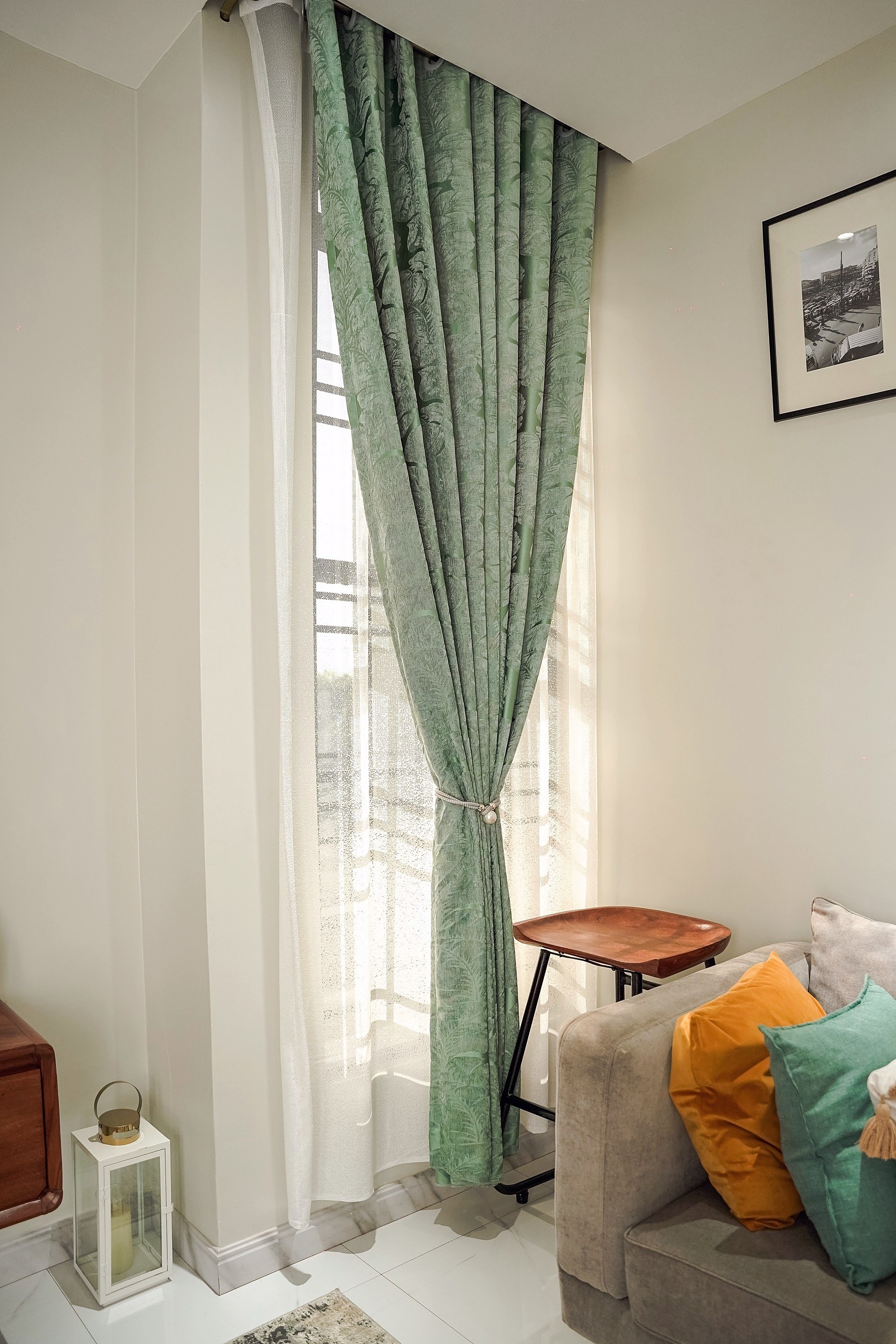 A wooden stool beneath a green curtain and a framed print