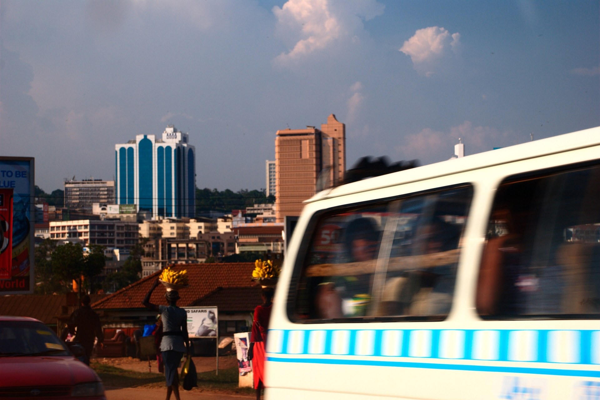 A white Kampala minibus taxi passing in front of the city skyline