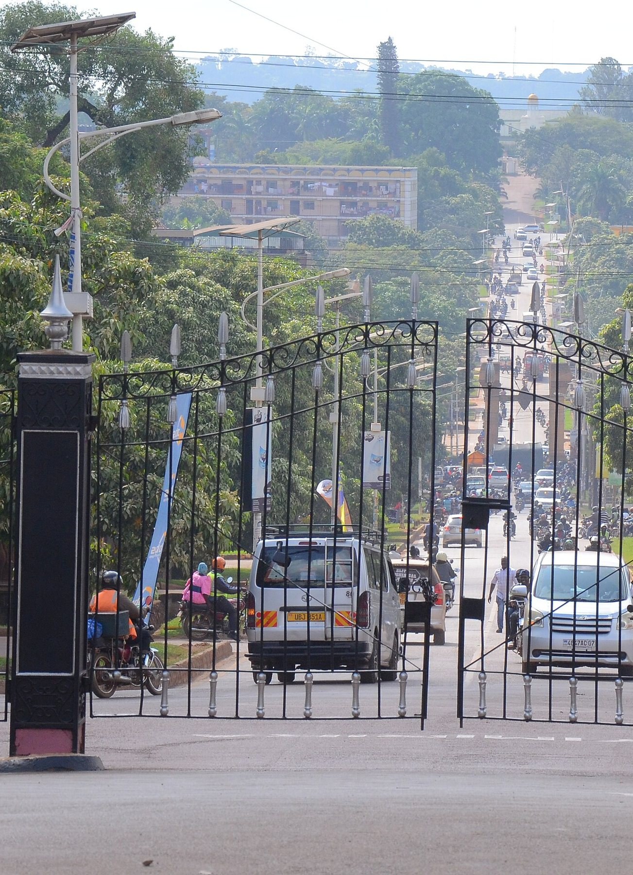 The Bulange gates opening onto the straight Kabaka Anjagala road, busy with cars and boda bodas, running up towards Mengo