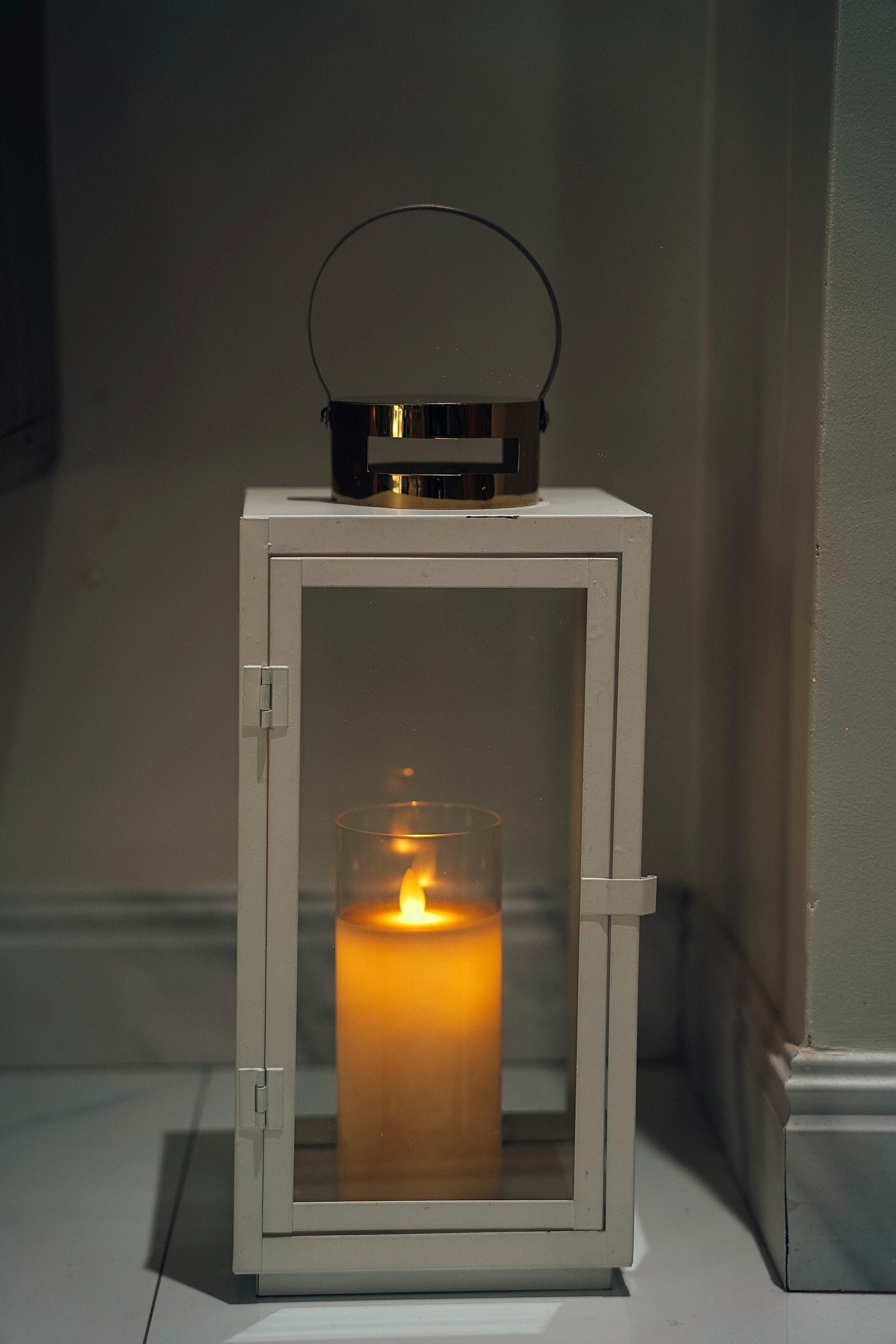 A white lantern with a lit candle by the window